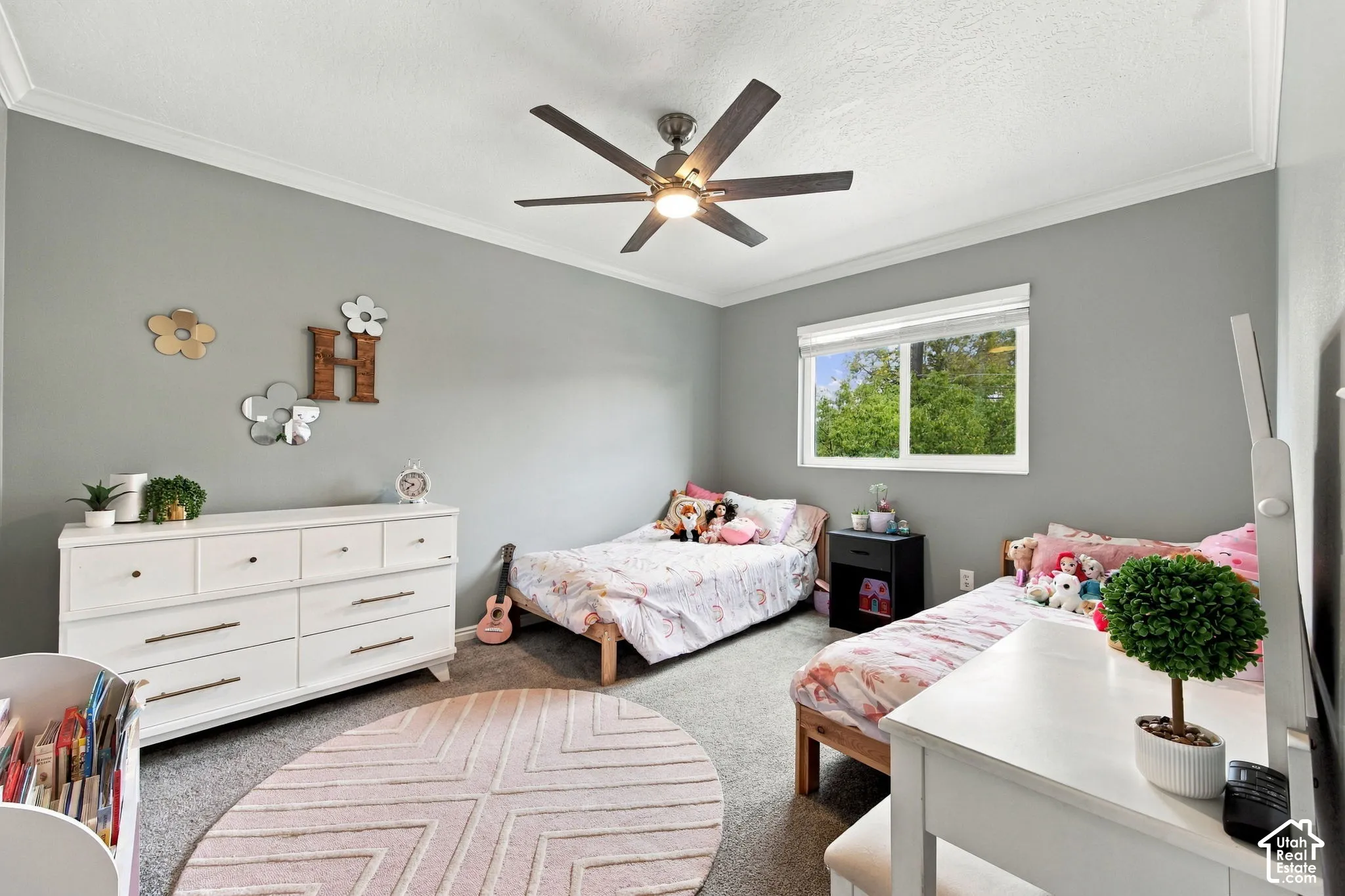 Neutral-toned interior featuring wall-to-wall carpeting, crown molding, a multi-blade ceiling fan with integrated lighting, and a dual-pane sliding window