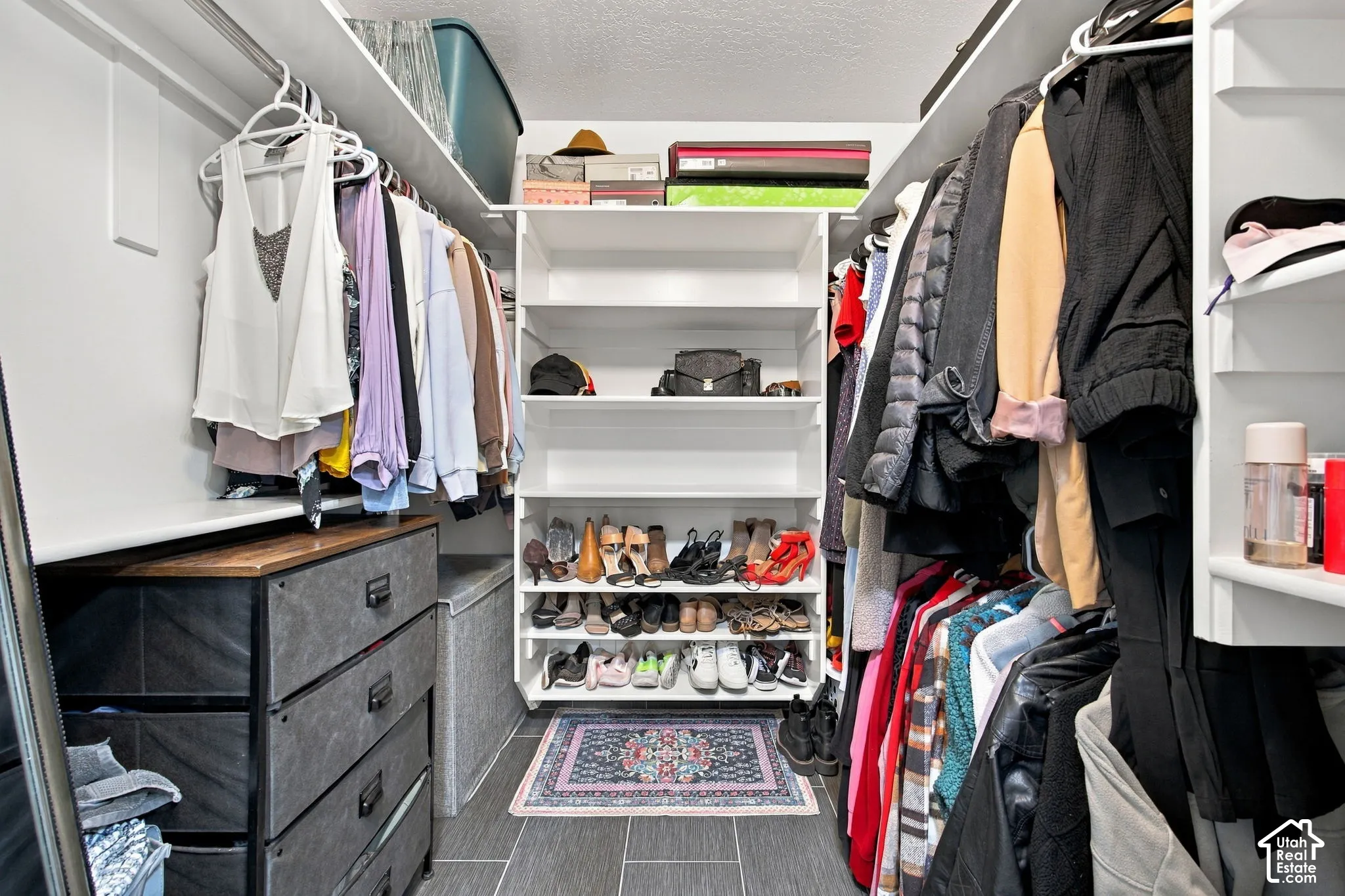 Walk-in closet featuring white built-in shelving, hanging rods, and large-format tile flooring