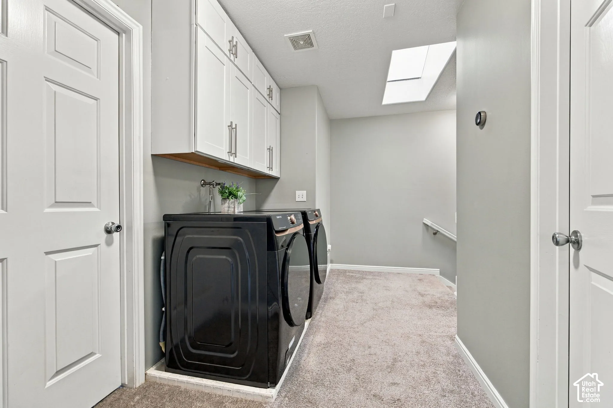 Utility space featuring white shaker-style wall cabinetry, a recessed skylight, neutral carpeting, and panel doors
