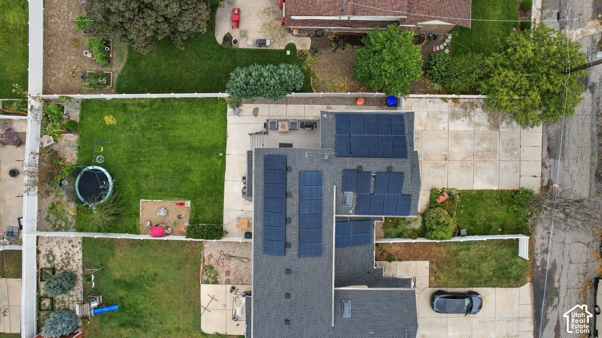 Aerial perspective of the property featuring a roof-mounted solar panel system, a concrete driveway, a rear deck, and a fenced backyard