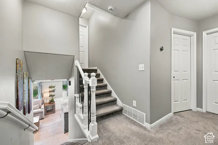 Staircase featuring a white balustrade with metal spindles, neutral carpeting, and solid-core paneled interior doors