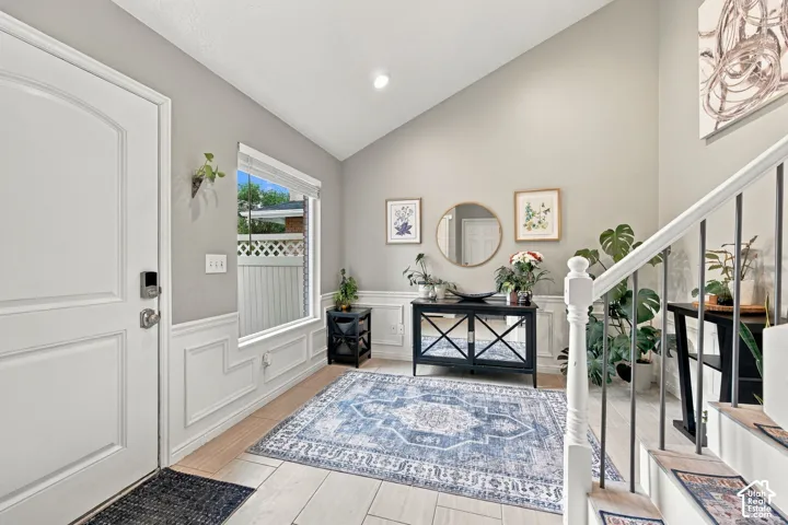 Entryway featuring vaulted ceilings, wainscoting, and light-toned tile flooring