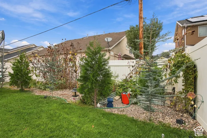 Backyard featuring a manicured lawn, stone-mulched landscape beds, established evergreen trees, and a white privacy fence
