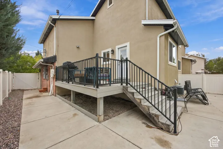 Stucco exterior featuring an elevated deck with black metal railing, concrete patio, and perimeter vinyl fencing