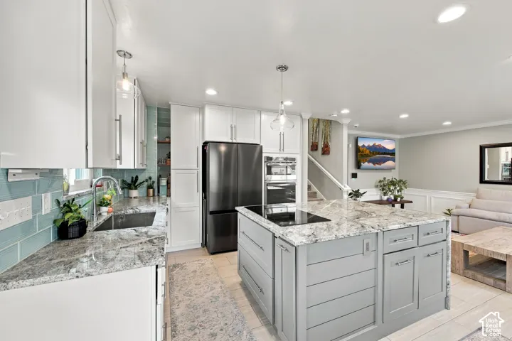 Kitchen featuring white cabinetry, stone countertops, a center island with built-in cooktop, tile backsplash, and stainless steel appliances