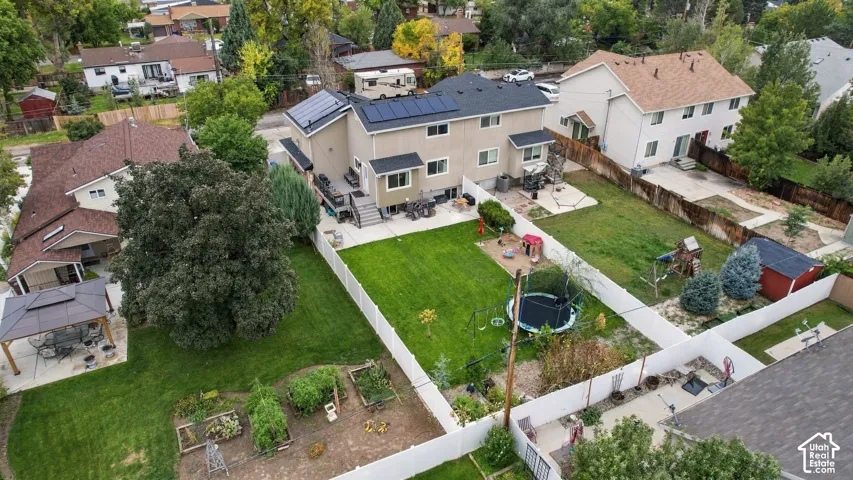 Two-story residence featuring rooftop solar panels, an elevated rear deck, a fenced backyard, and raised garden beds