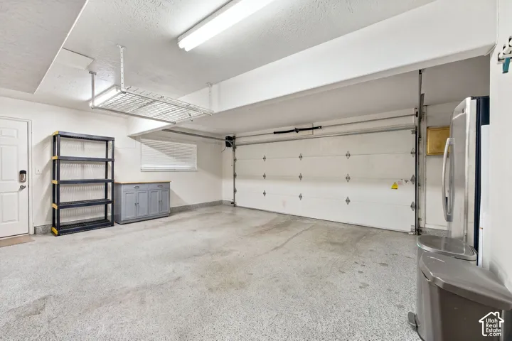 Garage interior featuring a concrete floor, a white sectional garage door, a ceiling-mounted storage rack, and a window with blinds