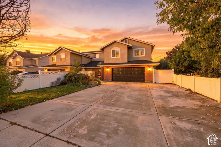Multi-level exterior featuring a two-car garage, brick and stucco siding, expansive concrete driveway, and full-perimeter vinyl fencing