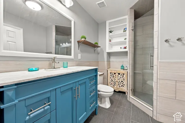 Bathroom featuring a dual-drawer vanity with a stone countertop, oversized wall mirror, walk-in glass-enclosed shower with tile surround, built-in shelving, and large-format tile flooring
