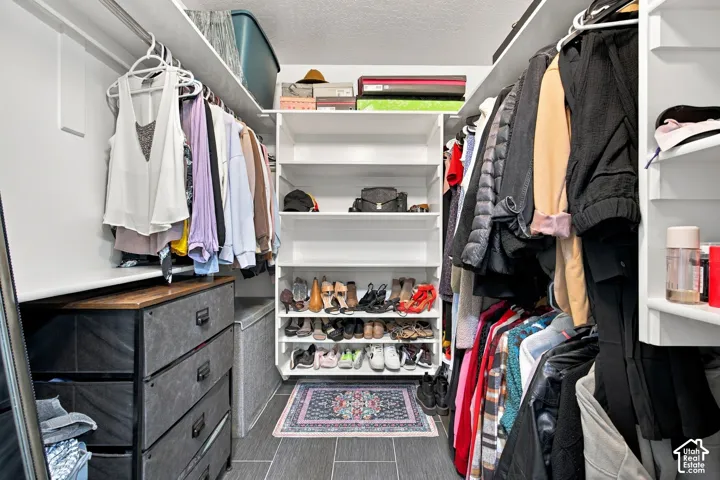 Walk-in closet featuring white built-in shelving, hanging rods, and large-format tile flooring