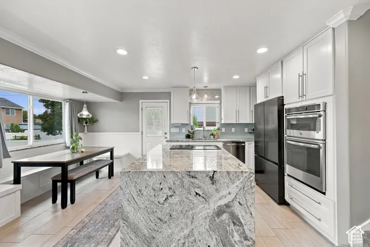 Kitchen featuring a large central island with stone countertop, white cabinetry, built-in double oven, recessed lighting, and wood-finish flooring
