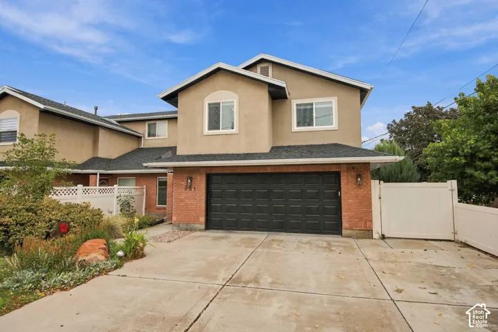 Two-story exterior featuring a brick and stucco facade, a double-car garage, and a concrete driveway, enclosed by white vinyl fencing