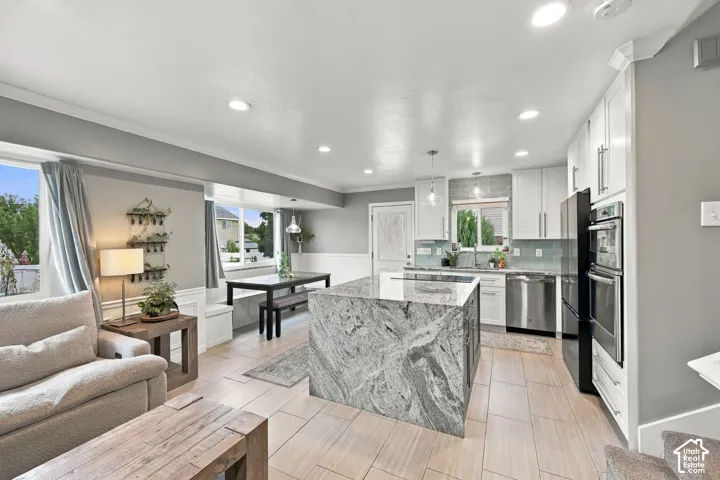Kitchen featuring an expansive center island with stone surfacing, white cabinetry, integrated stainless steel double wall ovens, tile flooring, and built-in window seating