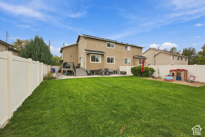 Fenced backyard featuring a manicured lawn, concrete patio, and structural exterior staircase