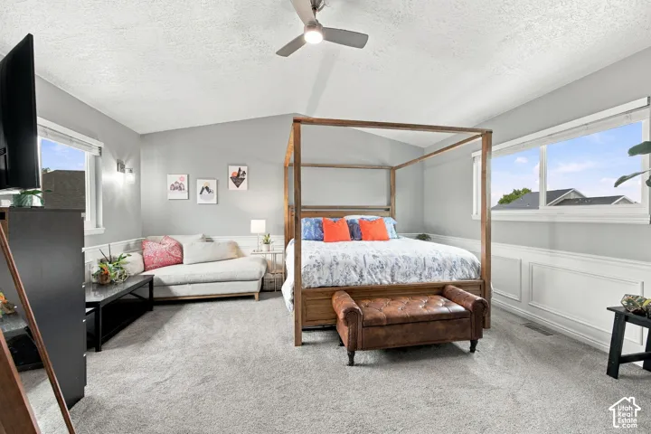 Vaulted ceilings, wainscoting wall paneling, neutral carpeting, and a ceiling fan with integrated lighting