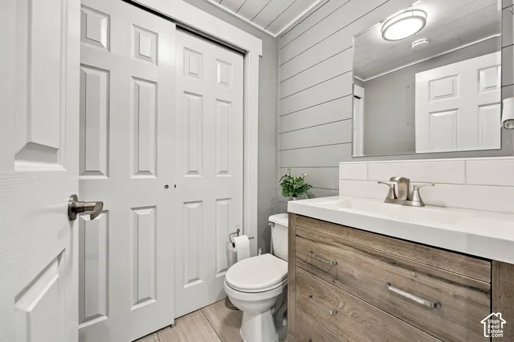 Vanity featuring a wood-finish cabinet, rectangular integrated sink, and brushed metal faucet, paired with horizontal plank wall paneling, a frameless mirror, and plank-style flooring
