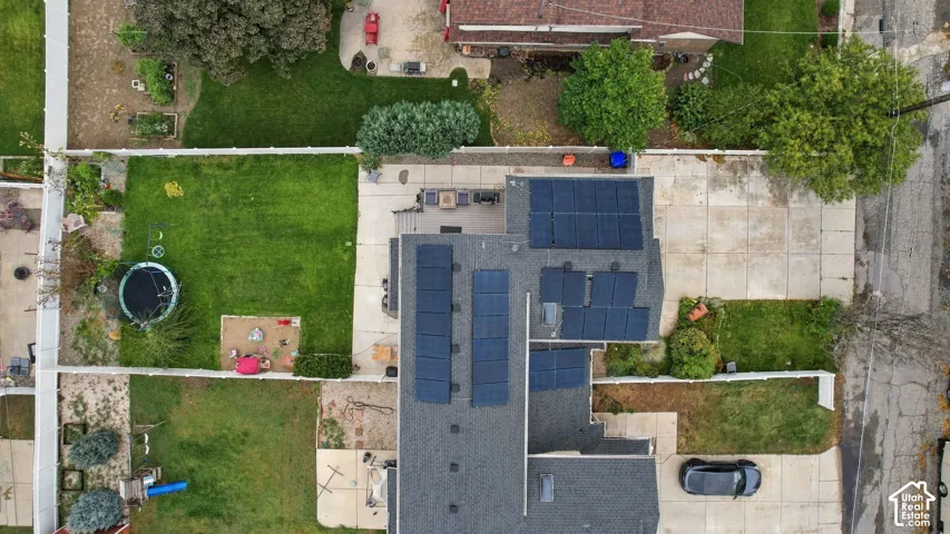 Aerial perspective of the property featuring a roof-mounted solar panel system, a concrete driveway, a rear deck, and a fenced backyard