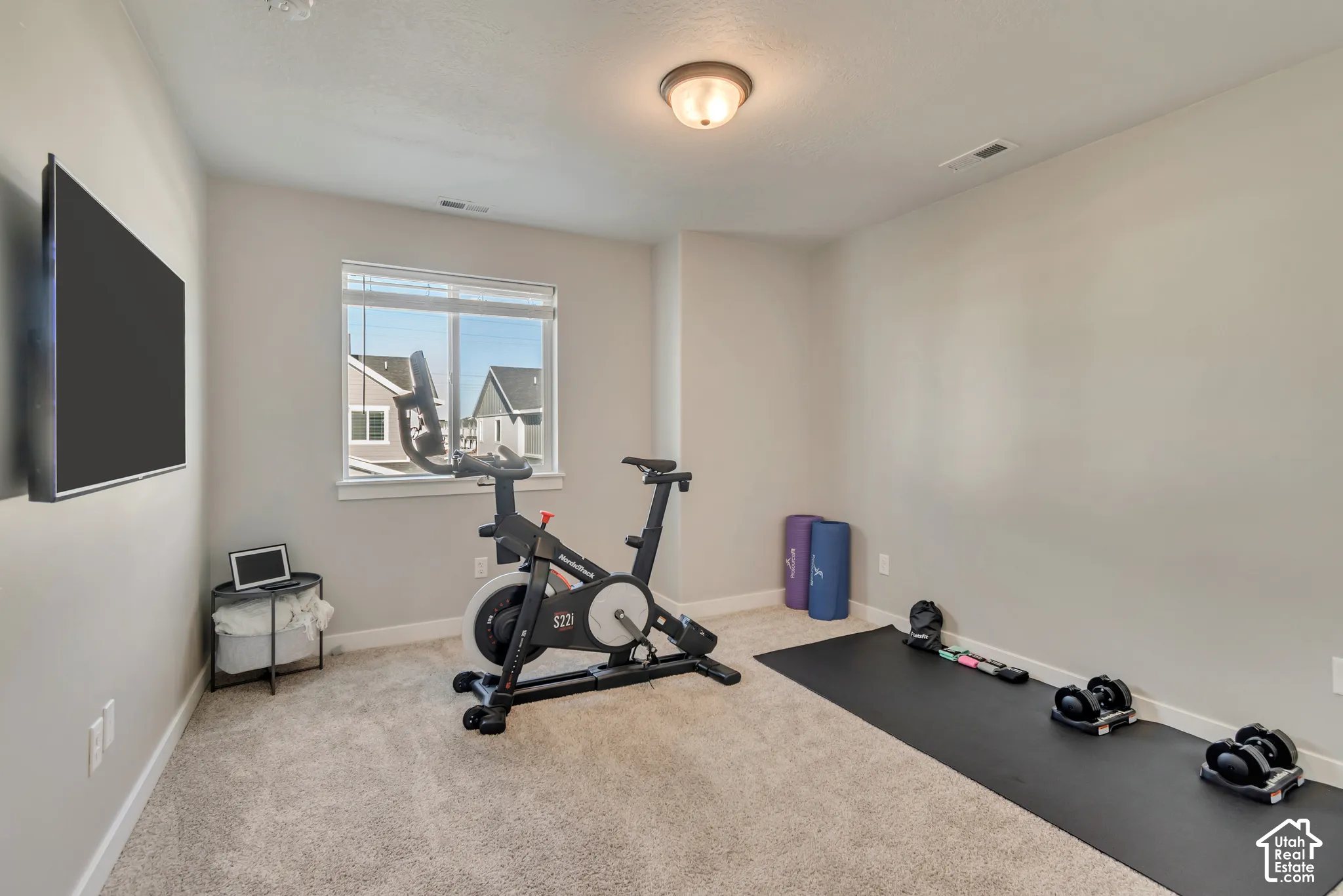 Recessed lighting, wall-mounted television, neutral carpeting, and a window with blinds
