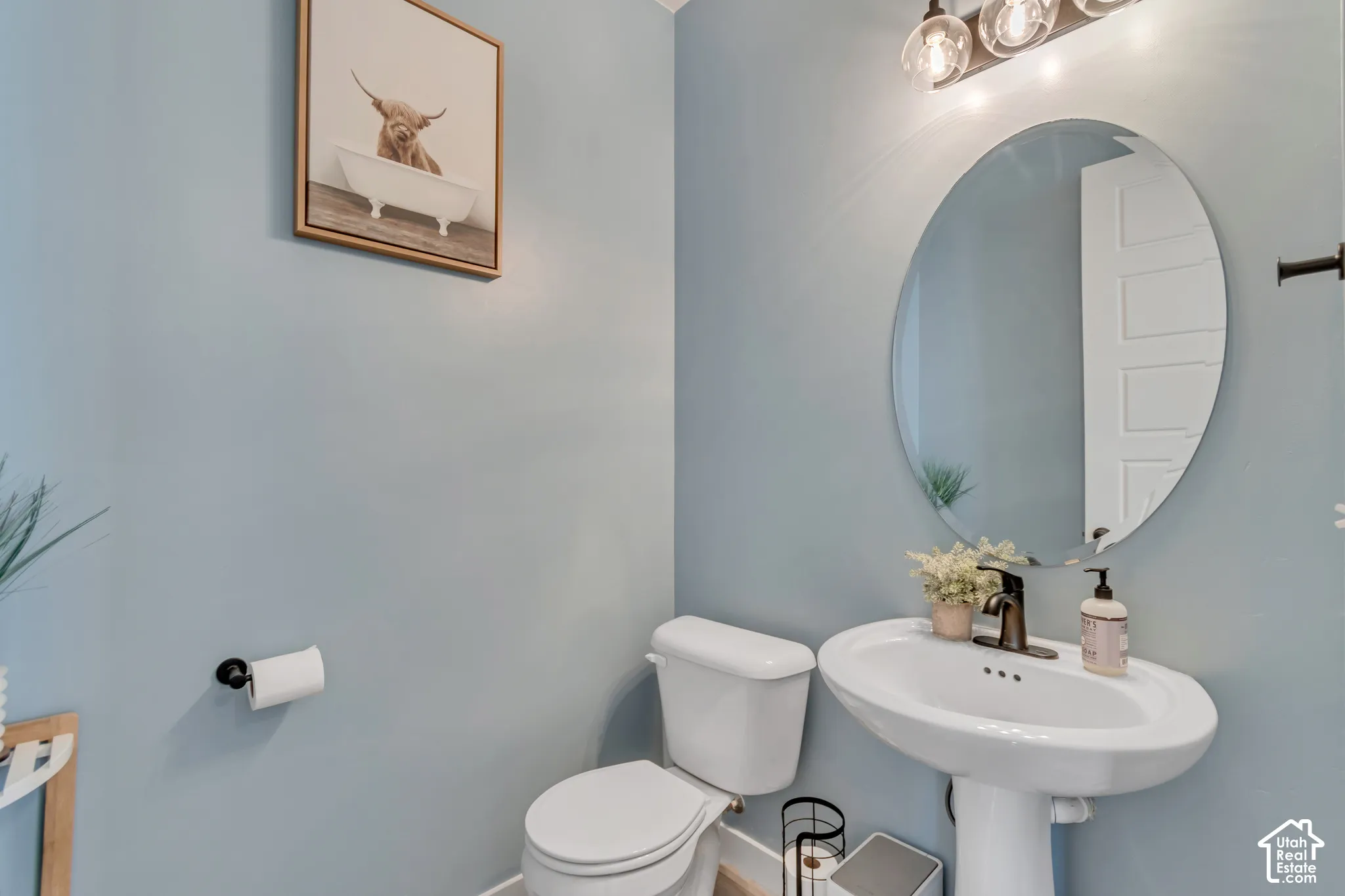 Pedestal sink with bronze-finish faucet, oval wall mirror, and three-light vanity fixture