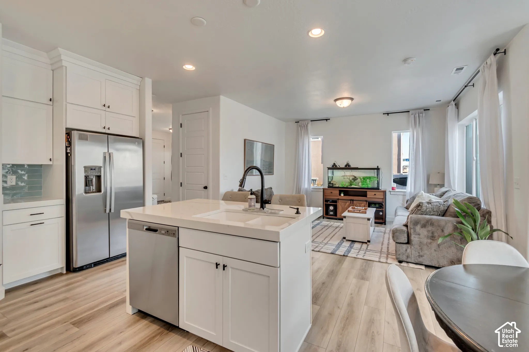 Open-concept kitchen and living area featuring wood-finish flooring, white cabinetry, and stainless steel appliances
