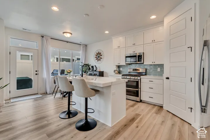 Kitchen featuring light wood-finish flooring, white cabinetry, stainless steel appliances, and a central island with a solid surface countertop
