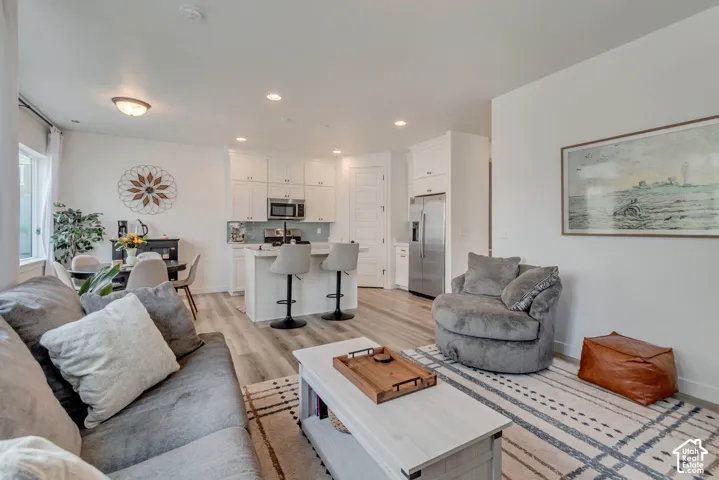 Open-concept living space featuring wood-finish flooring, recessed lighting, white cabinetry, and stainless steel appliances