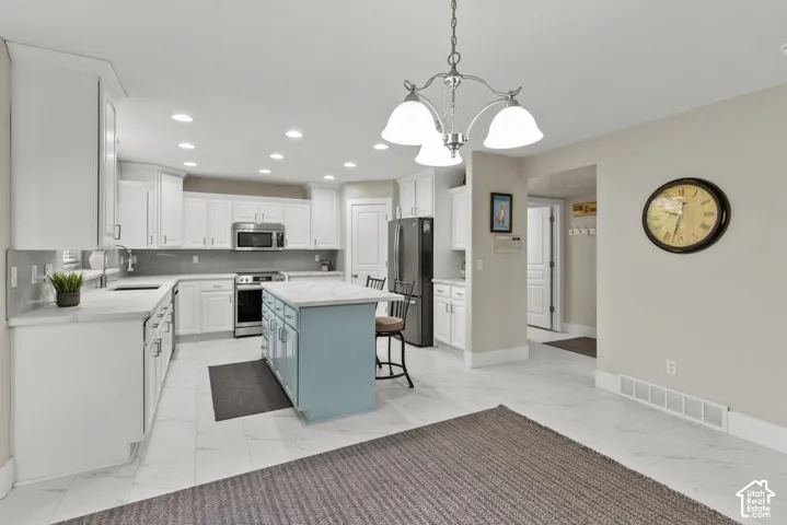 Kitchen featuring white cabinetry, a light blue central island with a stone-finish countertop, stainless steel appliances, recessed ceiling lighting, and tile flooring