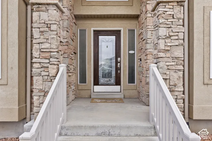 Entryway featuring stone veneer columns, a stained-wood door with a glass insert, side lights, and white railings