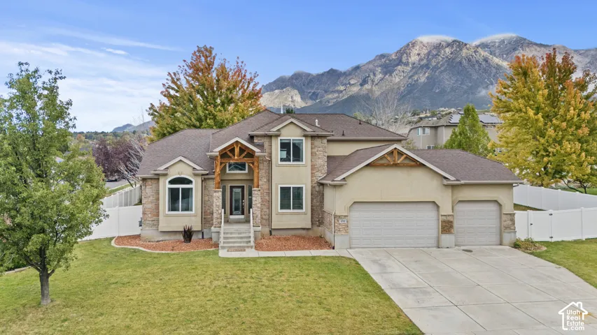 Two-story residence featuring a mixed stone and stucco exterior, prominent timber gabled entryway, three-car garage, and mountain backdrop