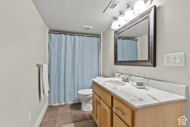 Bathroom featuring a wood vanity with a white countertop, oval undermount sink, framed mirror, and tiled flooring