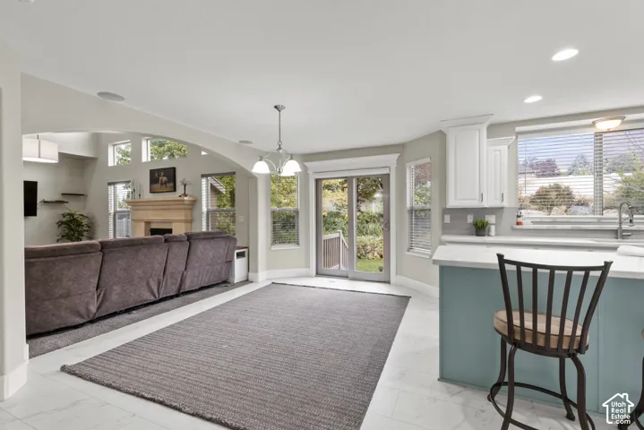 Open-concept interior featuring light tile flooring, arched wall detailing, a fireplace with a stone-finish surround, white cabinetry, and sliding glass doors