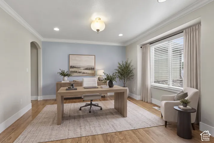 Room featuring wood-finish flooring, crown molding, an arched entryway, and a large window with recessed lighting