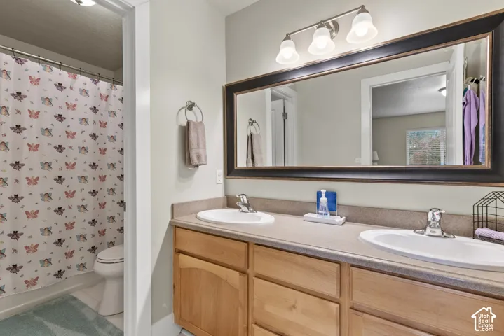 Dual-sink vanity with a solid-surface countertop, light wood-finish cabinetry, framed rectangular vanity mirror, and three-light fixture