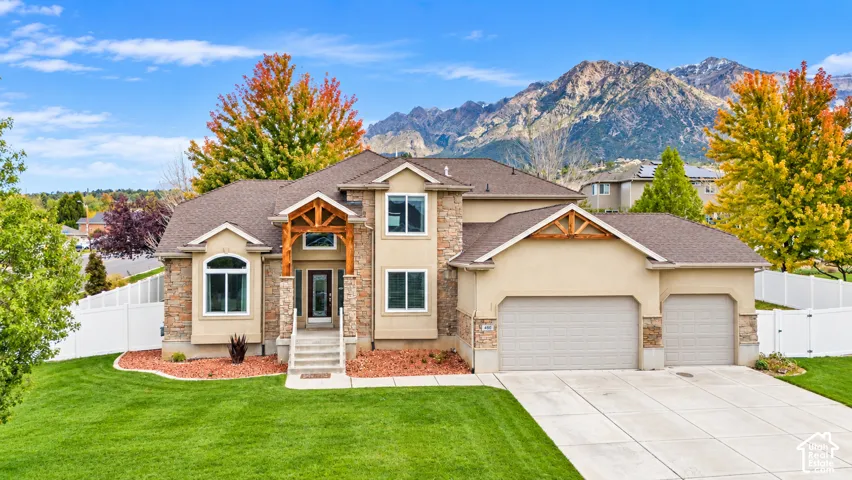 Multi-level residence featuring stone and stucco exterior, timber-frame entryway detail, mountain backdrop, three-car garage, and manicured lawn