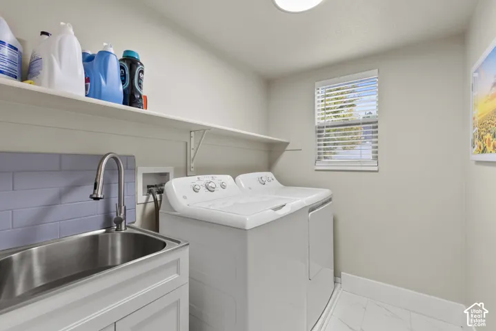 Utility room featuring a stainless steel drop-in sink, high-arc faucet, subway tile backsplash, white shaker-style cabinetry, and stone-finish flooring