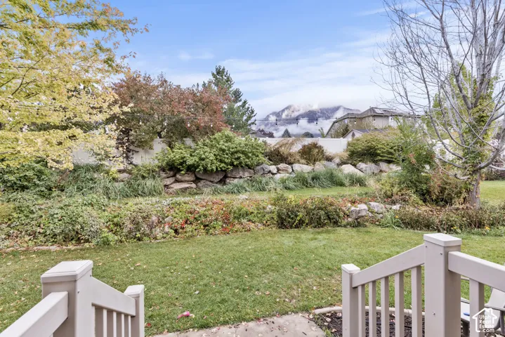 Backyard featuring a tiered stone retaining wall, manicured lawn, perimeter fencing, and mountain scenery