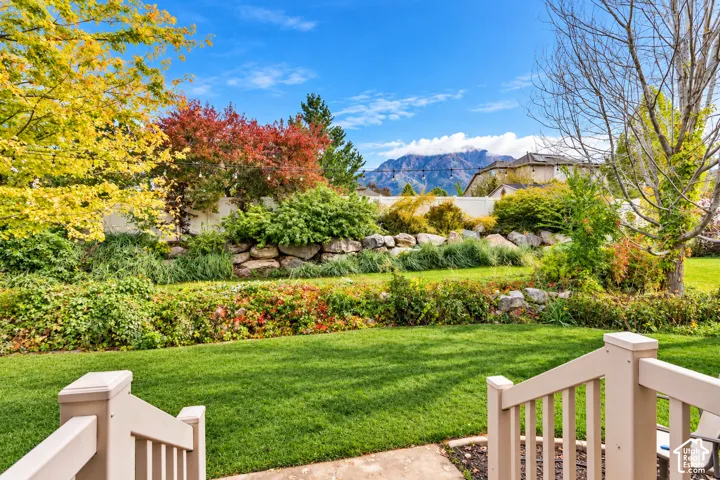 Backyard featuring a manicured lawn, tiered stone retaining wall, mature landscaping, and mountain backdrop