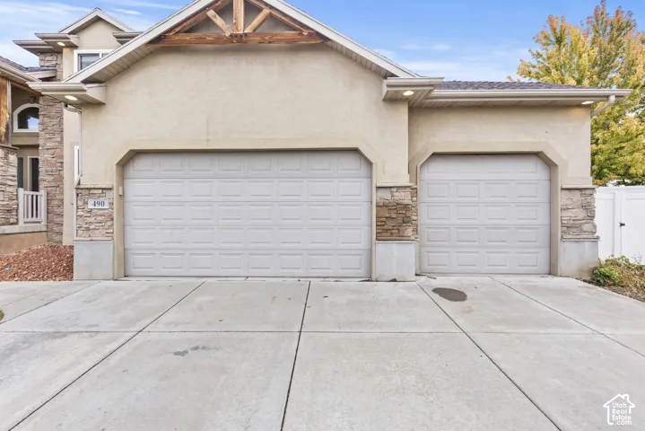 Stucco exterior featuring stone veneer accents, a triple-bay garage with paneled doors, and exposed wooden truss detailing