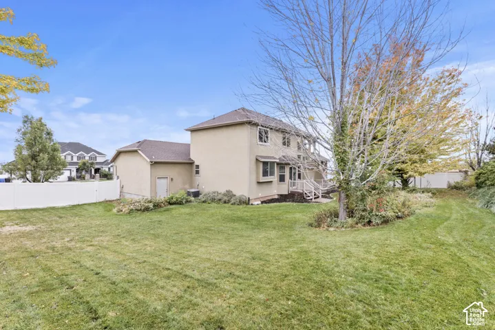 Expansive backyard featuring a manicured lawn, mature trees, privacy fencing, and exterior stucco siding