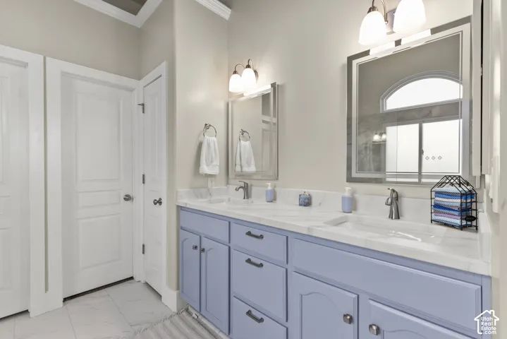Double vanity featuring a stone-look countertop, dual undermount sinks, crown molding, two framed mirrors, and brushed nickel fixtures