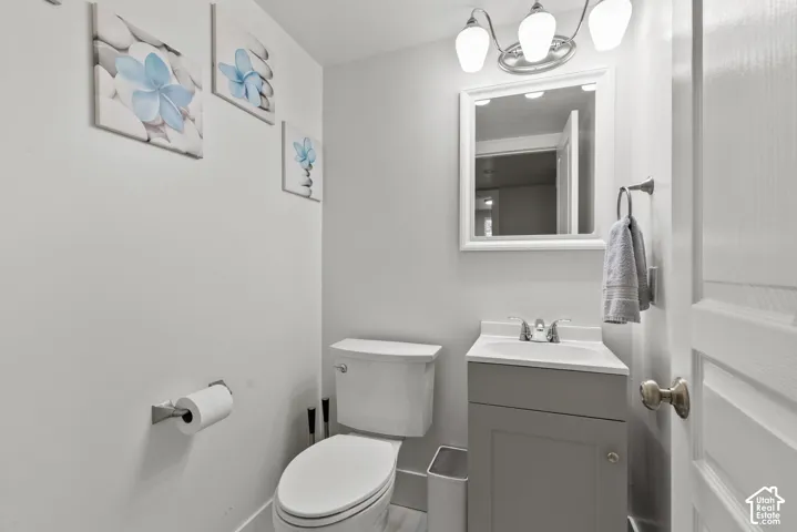 Bathroom featuring a grey shaker-style vanity, white countertop with an integrated sink, polished chrome faucet, framed vanity mirror, and a three-light fixture