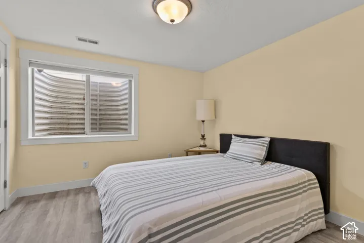 Neutral-toned bedroom featuring wood-finish flooring, a sliding window with a window well, and a flush-mount ceiling light