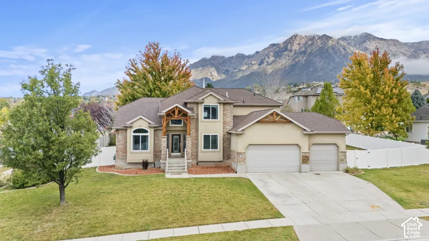 Two-story exterior featuring stone veneer accents, timber-frame gable detailing, a concrete driveway, a three-car garage, and a mountainous backdrop
