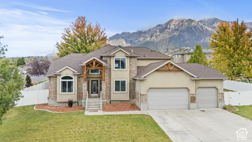 Exterior featuring a stone and stucco facade, timber-framed entryway, concrete driveway, attached three-car garage, and mountain backdrop