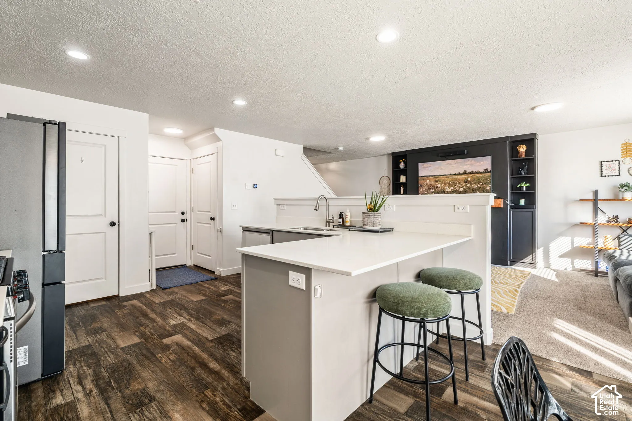 Kitchen featuring an island with a peninsula-style breakfast bar, quartz countertops, recessed lighting, and wood-finish flooring, complemented by built-in dark-toned shelving