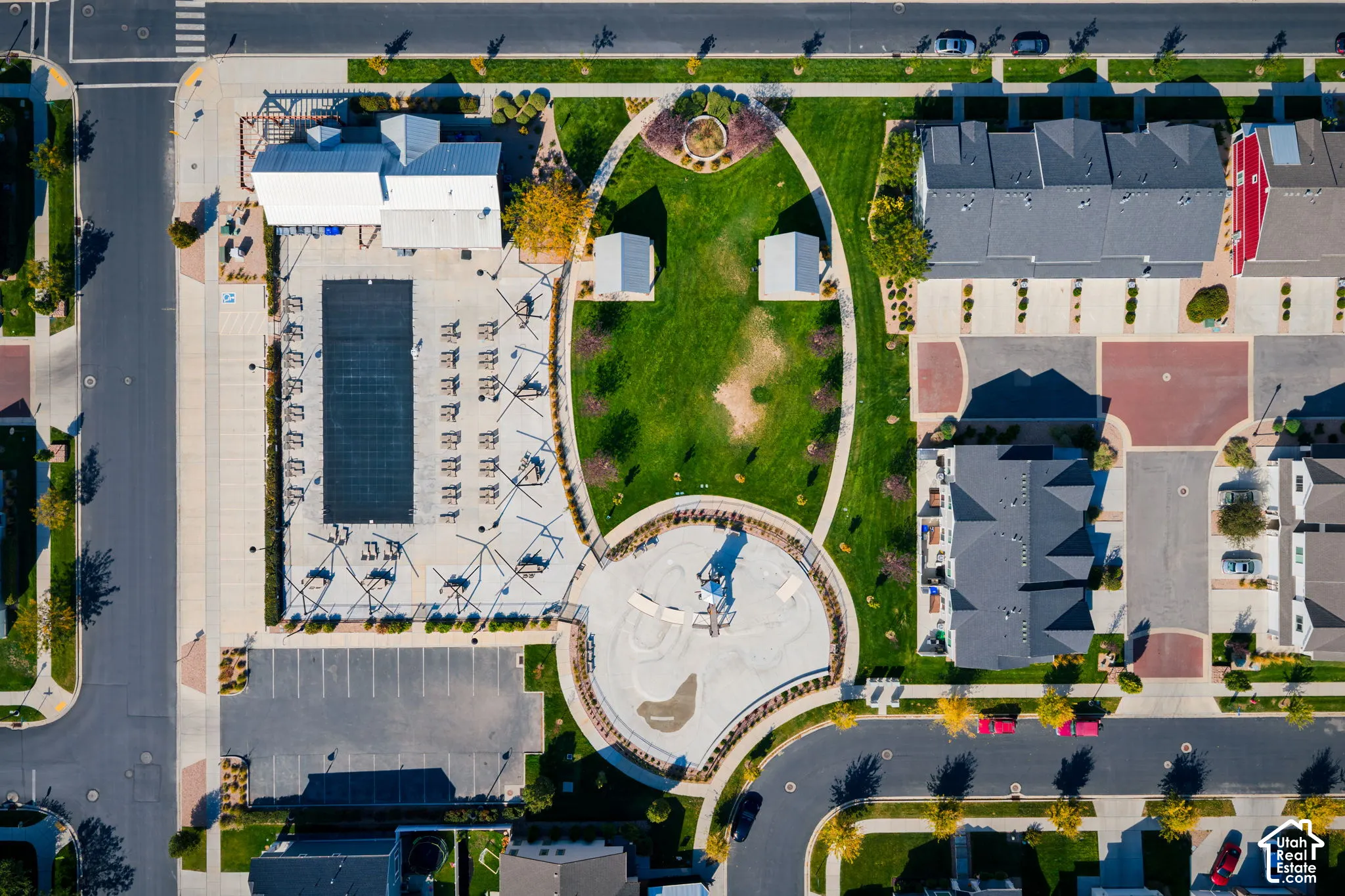 Aerial view of common area amenities featuring a swimming pool, paved parking lot, central lawn, and playground