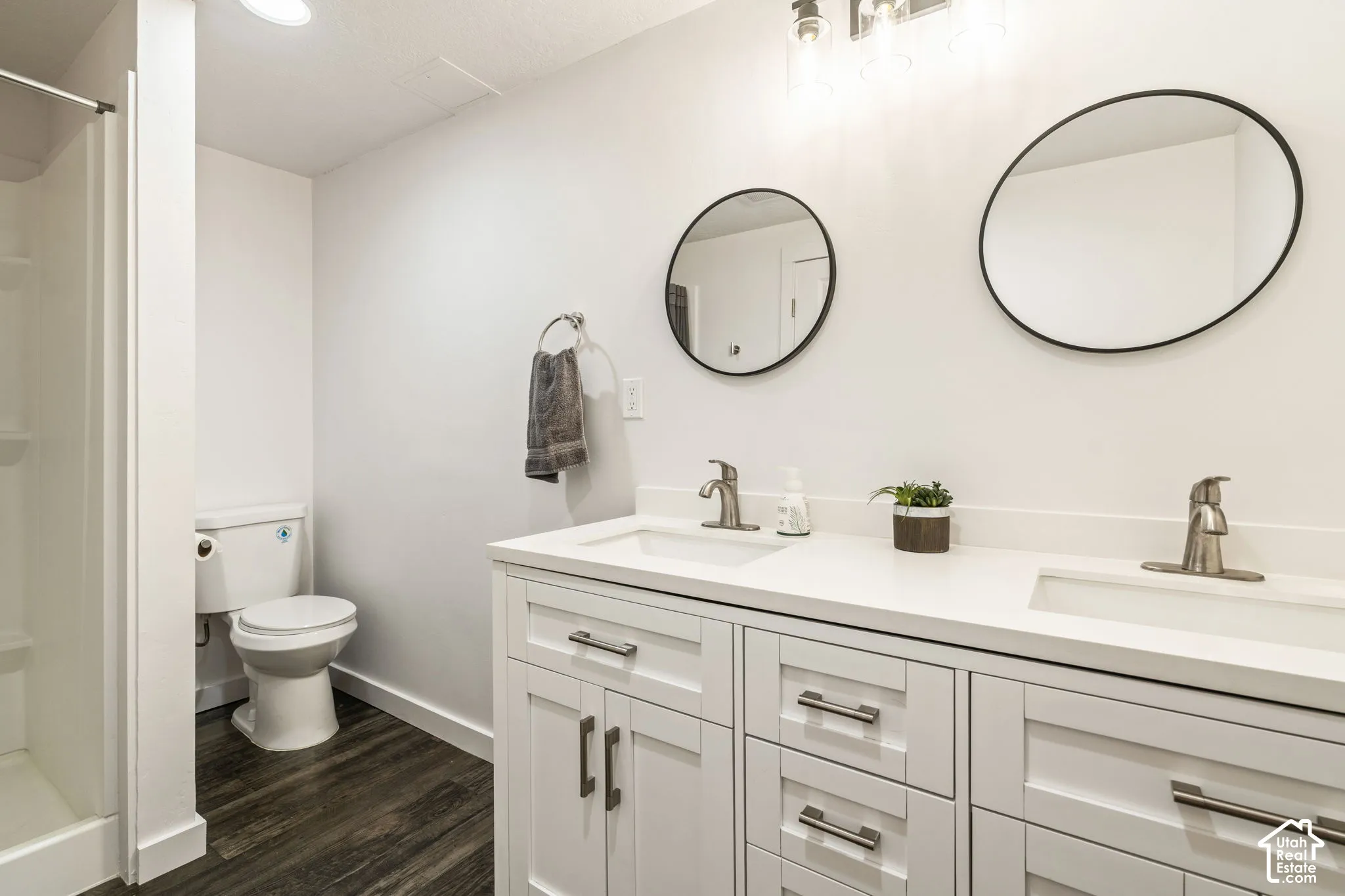 Double vanity featuring white cabinetry, a solid surface countertop with integrated dual sinks, brushed metal faucets, round wall-mounted mirrors, and wood-finish flooring