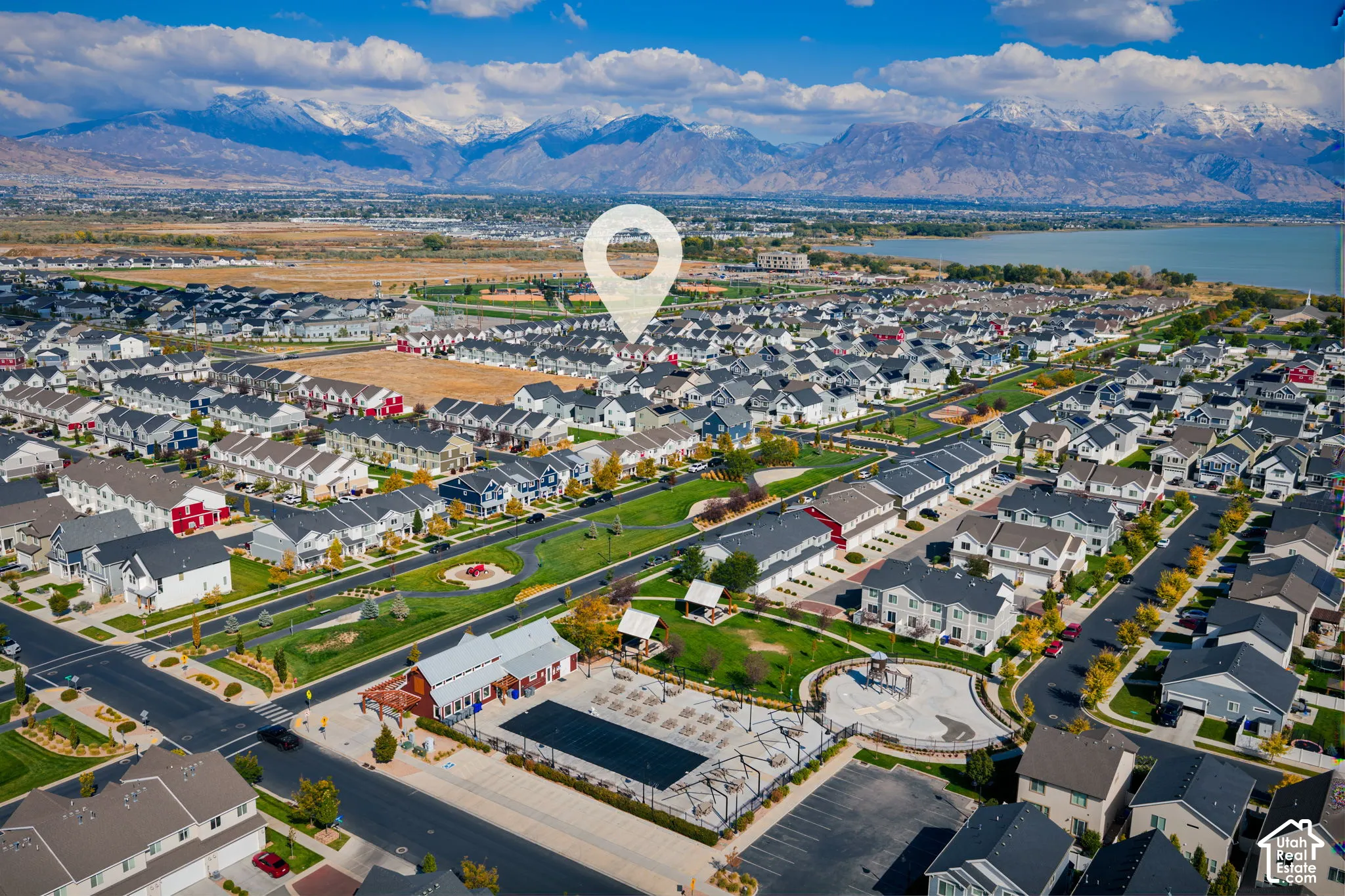 Aerial perspective of the residential community featuring mountain range backdrops, proximity to open water, expansive green space, and neighborhood amenities including a swimming pool and playground