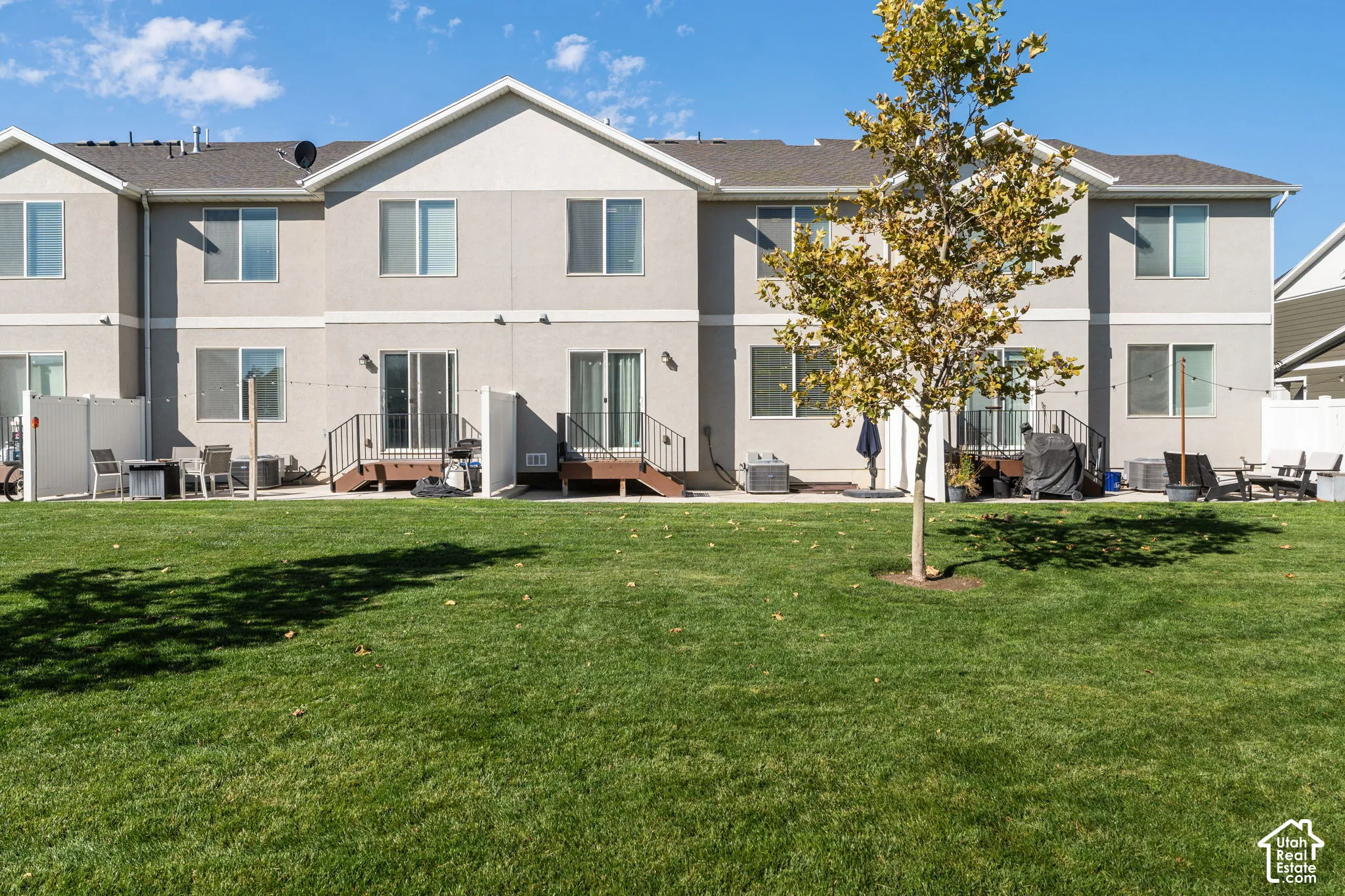 Multi-unit exterior featuring light-toned stucco siding, shared lawn space, concrete patio pads, and privacy fencing