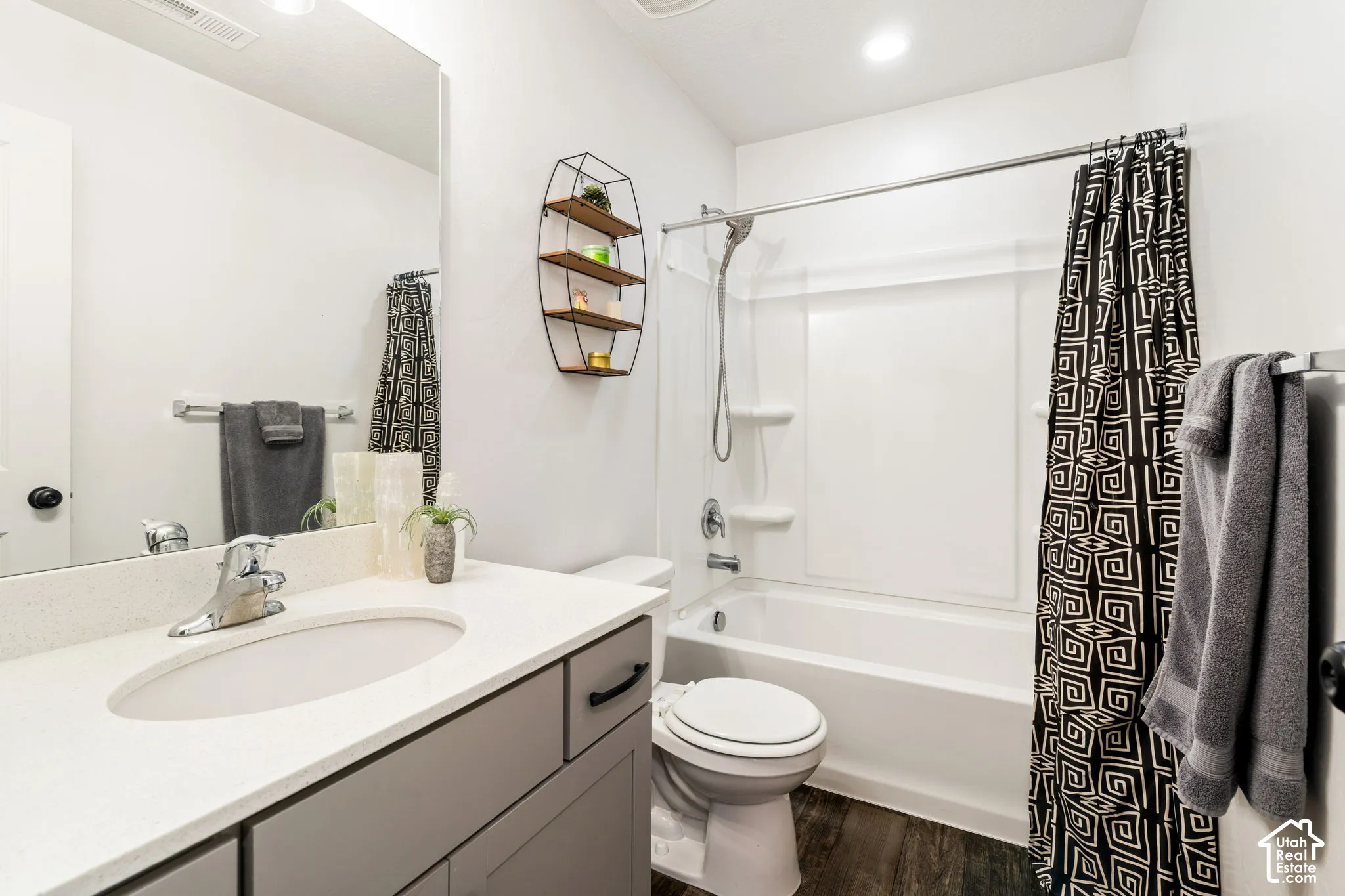 Bathroom featuring a grey vanity with a solid surface countertop, an undermount oval sink, chrome plumbing fixtures, and wood-finish flooring